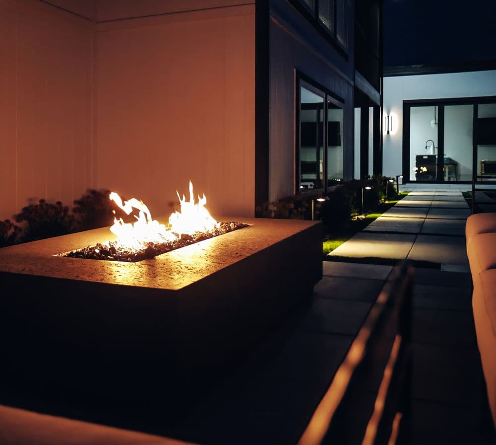 Modern outdoor fire pit at night, surrounded by sleek landscaping and patio furniture.