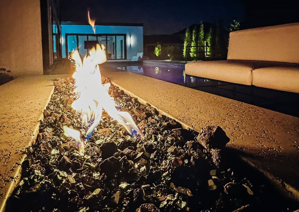 Modern outdoor fire feature with colorful flames beside a sleek pool at night.