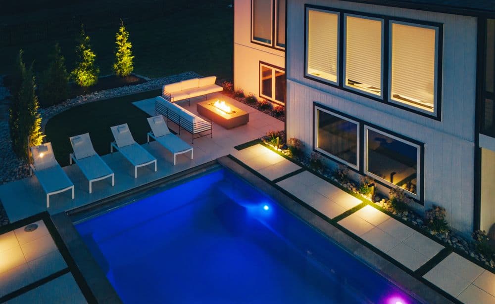 Luxury outdoor lounge area with pool, fire pit, and modern furniture at night.