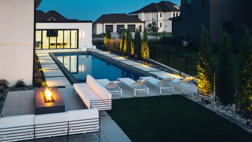 Modern backyard with a sleek pool, lounge chairs, and fire pit, surrounded by lush greenery.