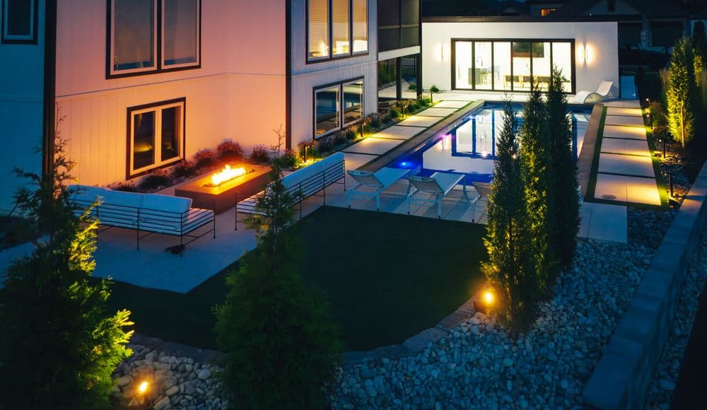 Modern backyard with pool, fire pit, and stylish seating illuminated at night.