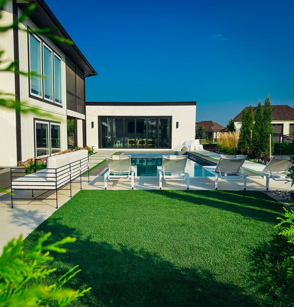 Modern backyard pool with lounge chairs and lush greenery, ideal for relaxing and entertaining.