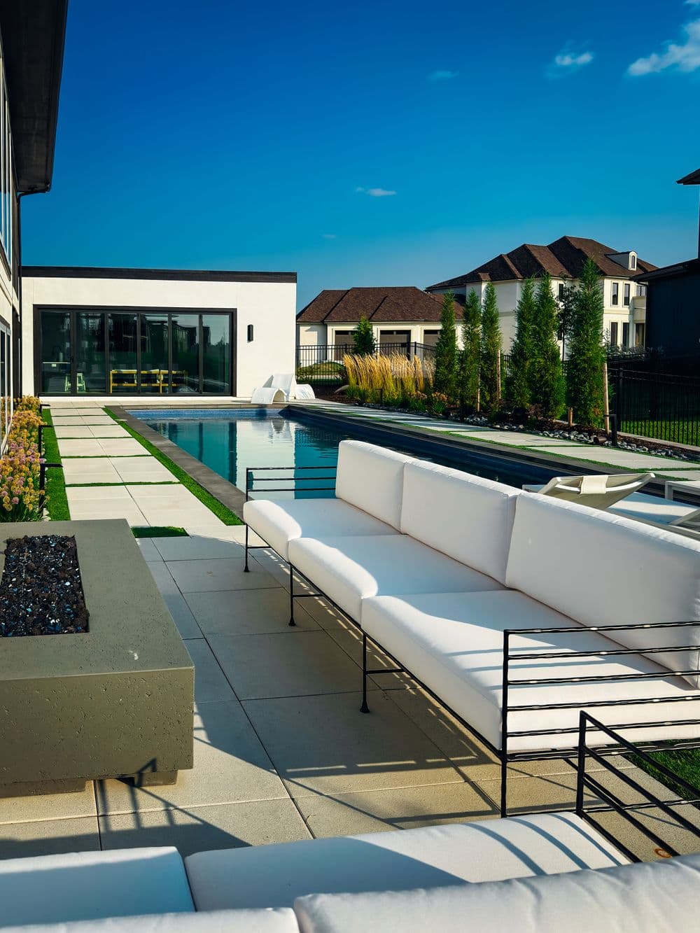 Modern outdoor living space featuring a sleek pool, white lounge seating, and lush landscaping.