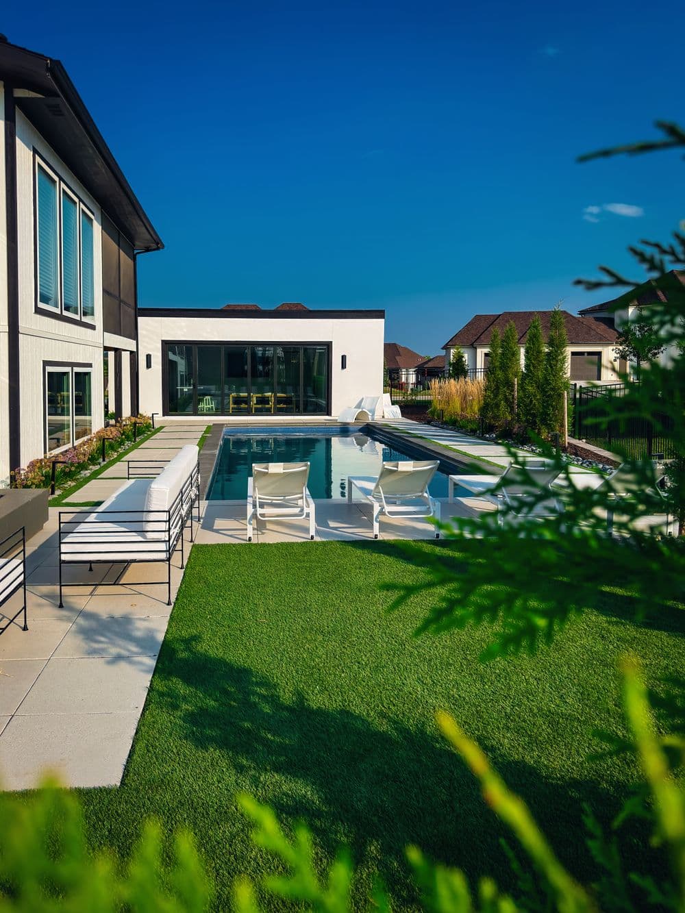 Modern home with a luxurious pool, sun loungers, and landscaped garden under a clear blue sky.