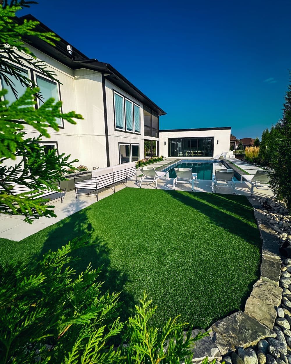 Modern home with pool, landscaped yard, and lounge chairs under a clear blue sky.