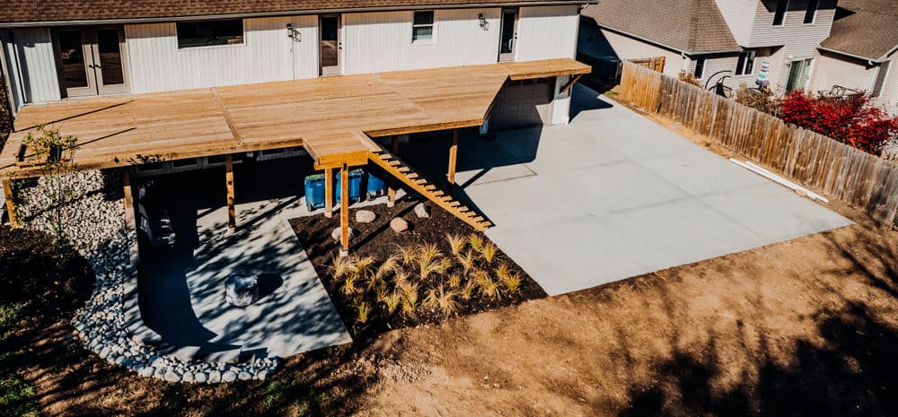 Wooden deck with stairs, landscaped yard, and driveway beside a modern home.