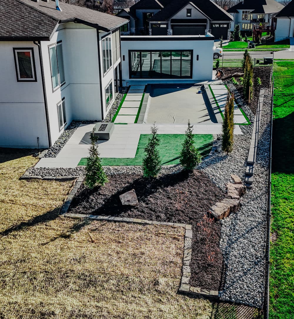 Modern home exterior with landscaped yard featuring artificial turf, patios, and garden beds.