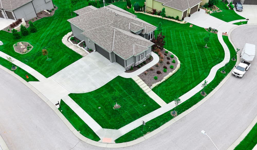 Aerial view of a modern house with landscaped yard and curved driveway in a suburban neighborhood.