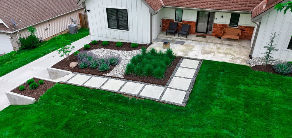 Aerial view of a home with landscaped yard featuring stones, grass, and patio seating area.