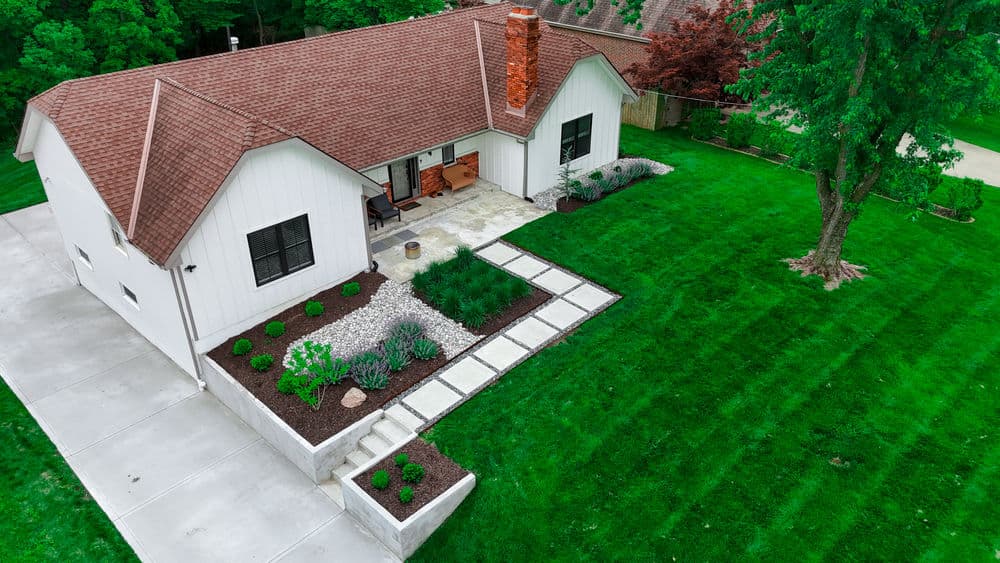 Aerial view of a modern house with landscaped yard and patio set in a green environment.