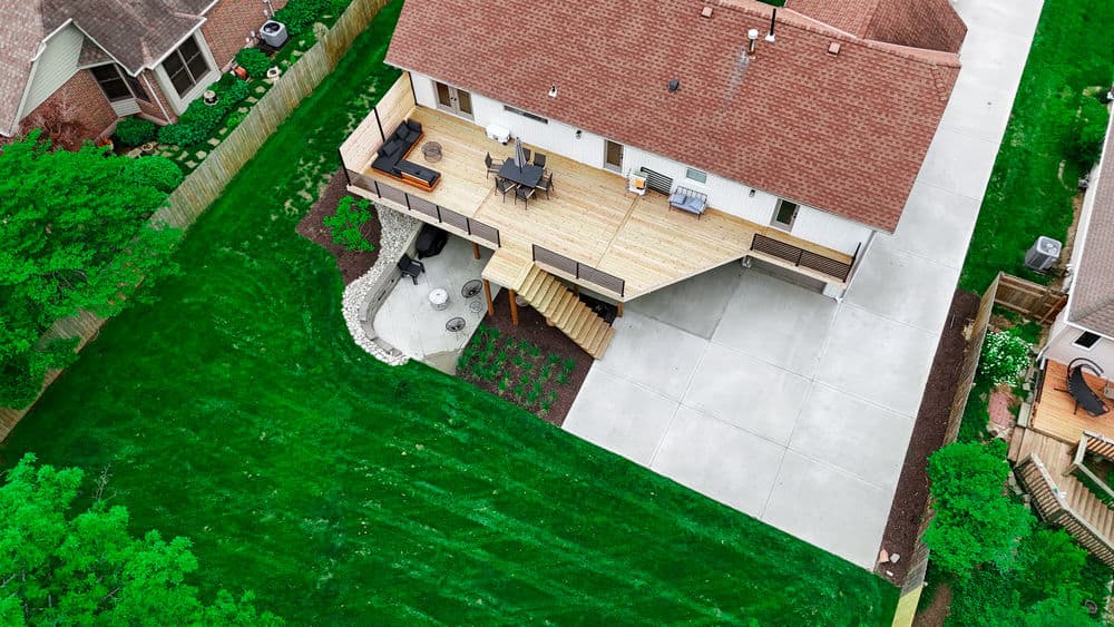 Aerial view of a house with a wooden deck, surrounded by green lawn and garden.