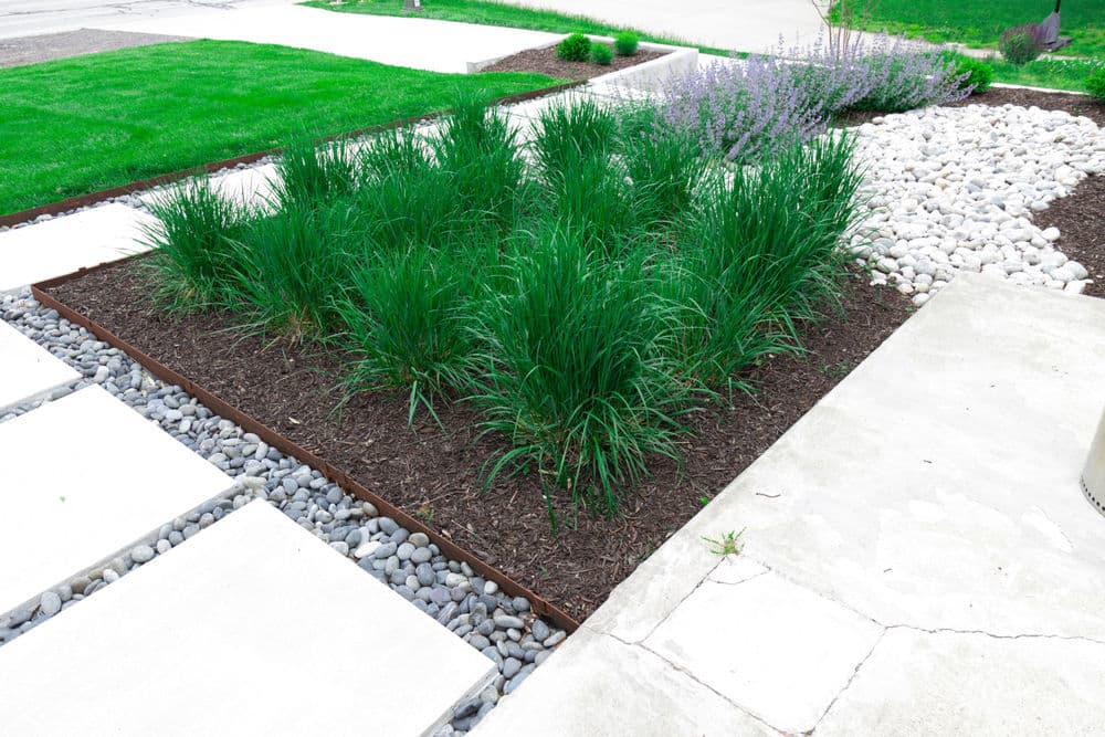Lush green grass and mulch landscaping with gravel and stone pathways in a garden setting.