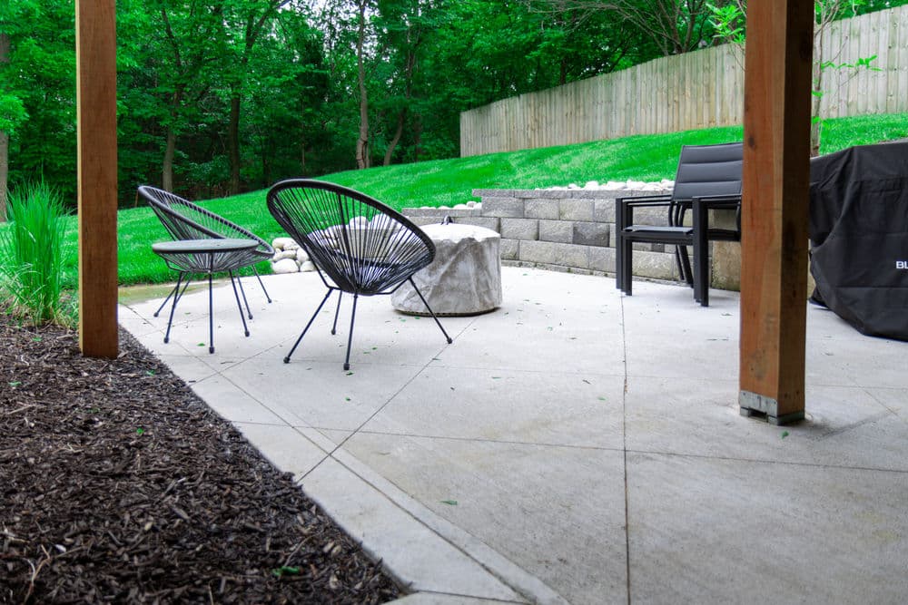 Outdoor patio with modern chairs, fire pit, and lush green landscaping in a serene setting.